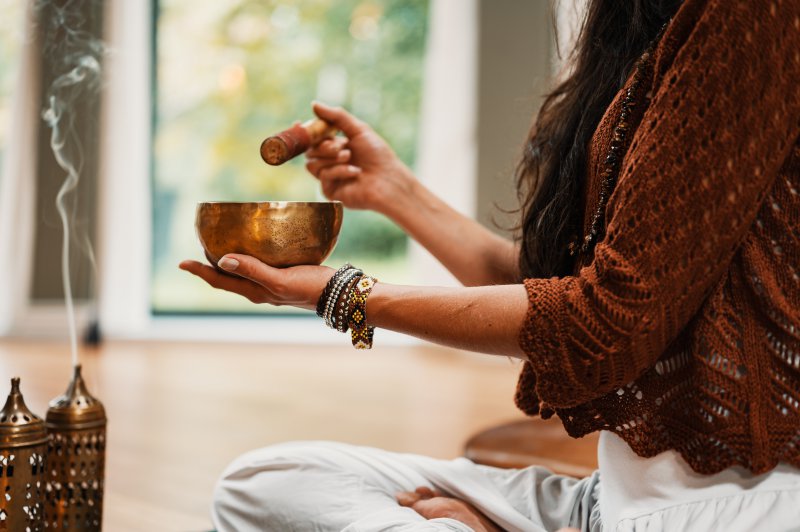 Frau im Lotossitz auf Meditationskissen mit Räucherstäbchen und Klangschale