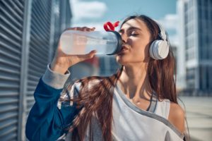 Eine Frau mit Over-Ear Bluetooth-Kopfhörern trinkt Wasser im freien