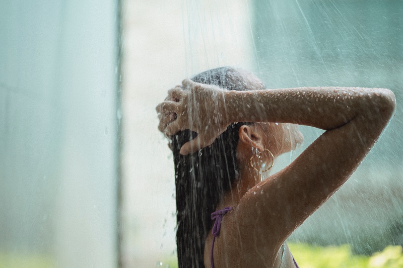 Frau wäscht Haarkur mit Wasser aus