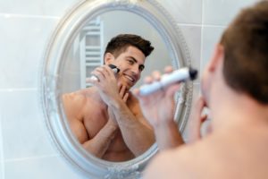 Mann rasiert sich mit elektrischen Rasierer vor einem Spiegel
