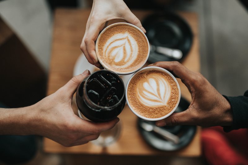Drei Menschen stoßen mit Kaffee an