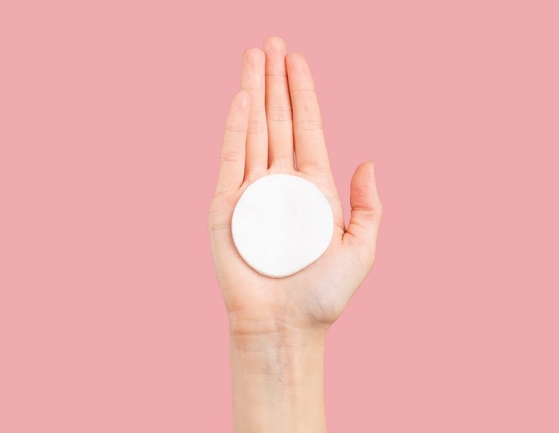 Auf einem rosa Hintergrund ist eine Hand welche ein waschbares Abschminkpad hält zu sehen