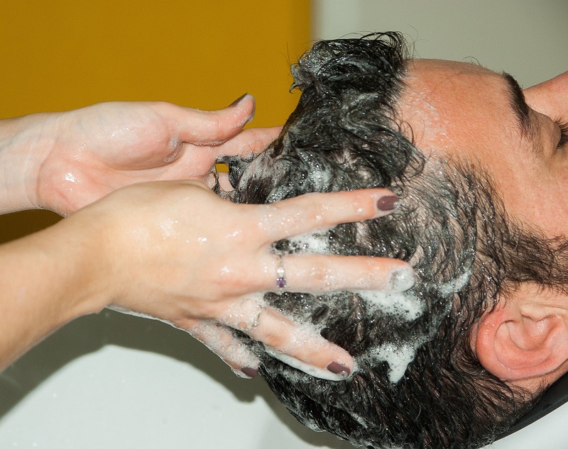 Einem Mann werden die Haaren gewaschen und eine schaumige Haarkur wird in seinen Haaren verteilt.