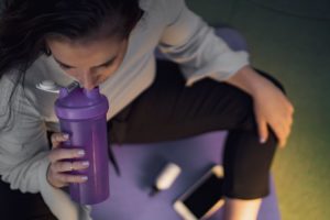 Frau, die sitzt und aus einem Protein Shaker trinkt