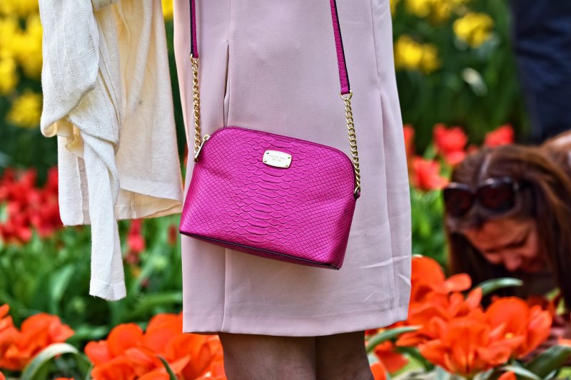 Eine Frau trägt eine teure Handtasche in einem knalligen Rosa.