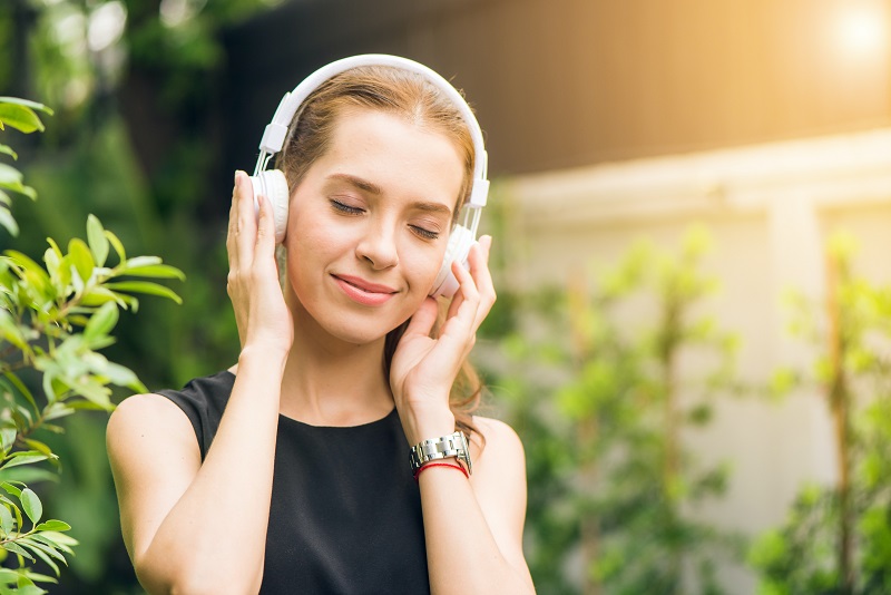 Frau entspannt mit Bluetooth Kopfhörern Frau mit over-ear Bluetooth-Kopfhörern entspannt im grünen