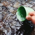 grüne Campingtasse wird zum Schöpfen von Wasser verwendet