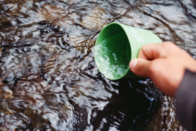 grüne Campingtasse wird zum Schöpfen von Wasser verwendet