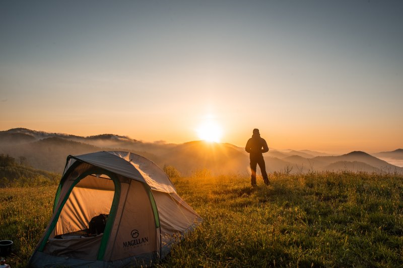 Einmannzelt neben einem Backpacker bei Sonnenuntergang