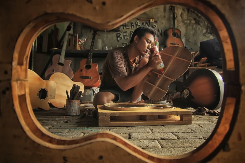 Ein Mann sitzt in einer Werkstatt und ist dabei eine Konzertgitarre zu bauen