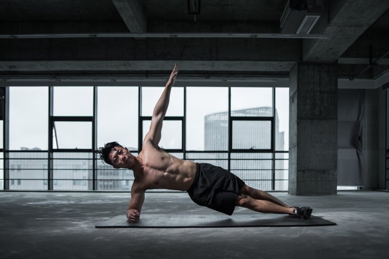 Training auf der Yogamatte Ein Mann macht einen seitlichen Unterarmstütz auf seiner Sportmatte