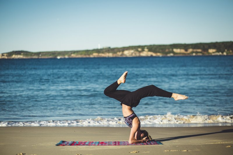 Frau macht Yoga am Meer mit bunter Yogadecke 