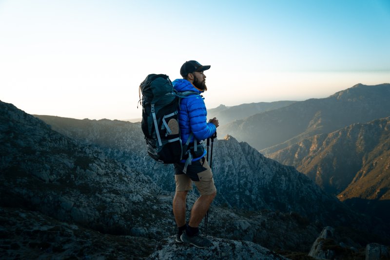 Mann steht mit einem Tourenrucksack auf einem Berg Tourenrucksäcke eignen sich auch für Bergwanderungen