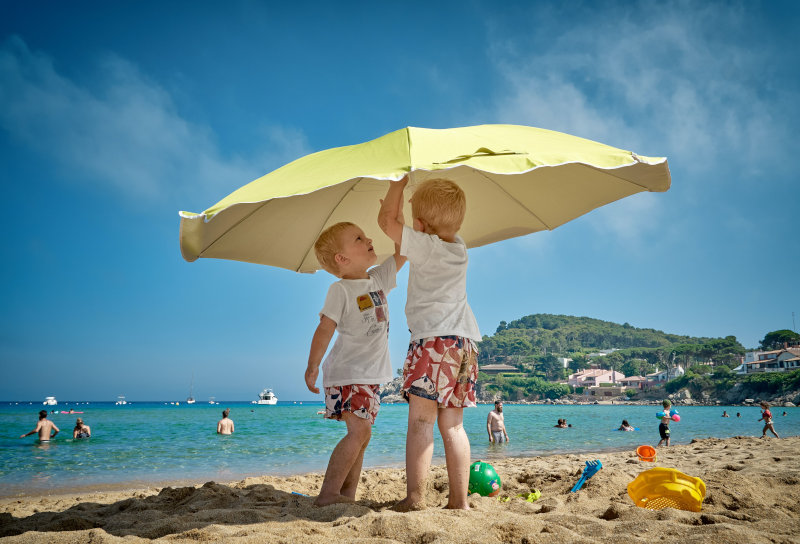 Zwei Kinder mit einem Sonnenschirm Zwei Kinder stehen unter einem Strandschirm