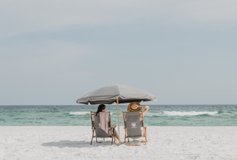Zwei Frauen sitzen am Strand auf Stühlen unter einem Strandschirm